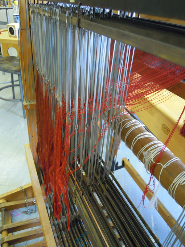 Here are warp threads pulled through the eyes of heddles on their corresponding harnesses.